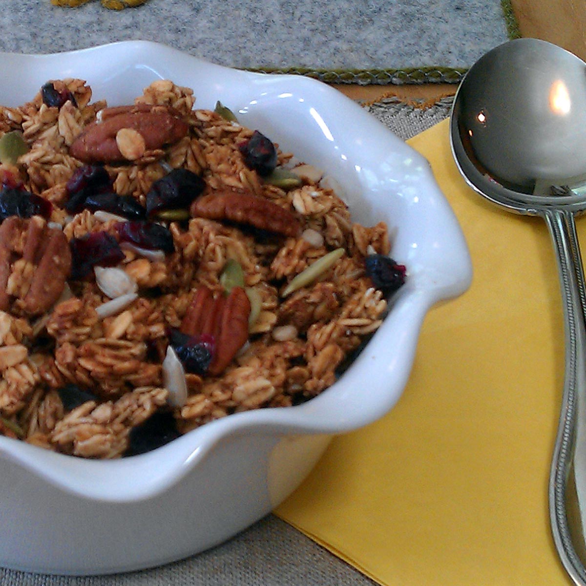 A white bowl of pumpkin seed granola next to a spoon and napkin