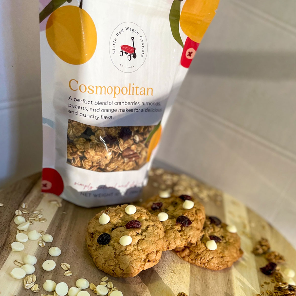 a bag of Little Red Wagon's Cosmopolitan granola flavor on a cutting board with cranberry christmas cookies surrounding it.